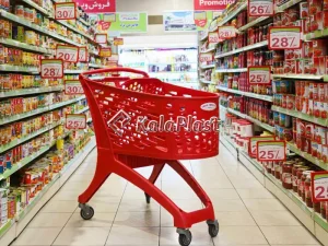 سبد خرید چرخدار فروشگاهی قرمز در راهروی سوپرمارکت میان قفسه‌های کالا